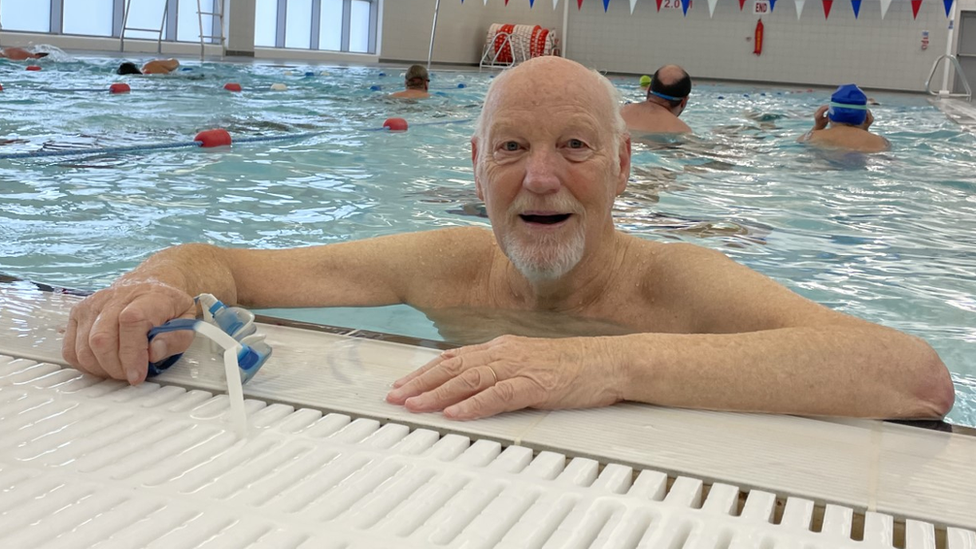 Bob Young at the shallow end of the pool with his arms in the air, smiling and wearing goggles.