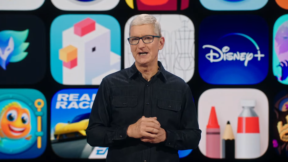 Tim Cook stands in front of a grid of app images on stage