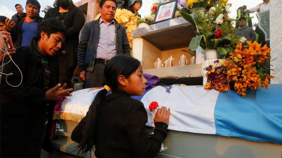 A girls holds a flower in front of the coffin with the body of a migrant killed in the Mexican state of Tamaulipas while trying to reach the US in January