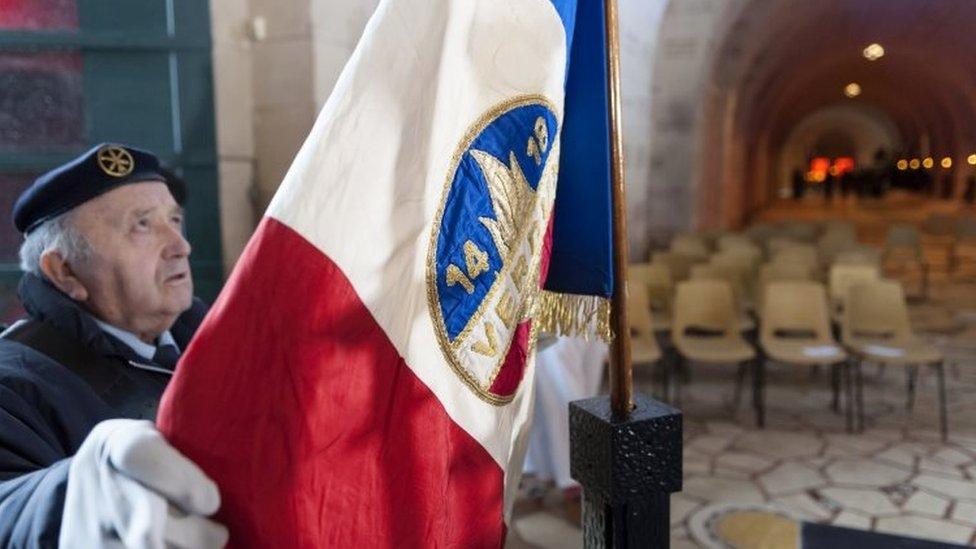 A military veteran unfurls a flag during a religious ceremony marking the centenary of the beginning of the battle of Verdun (21 February 2016)