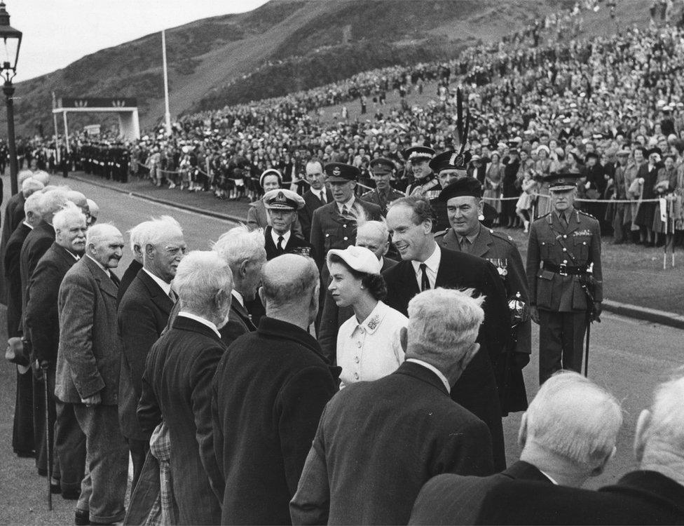 In 1952, Queen Elizabeth receives Scots veterans of the 'Wet Review' of 1881, when the entire company was drenched while receiving Queen Victoria.