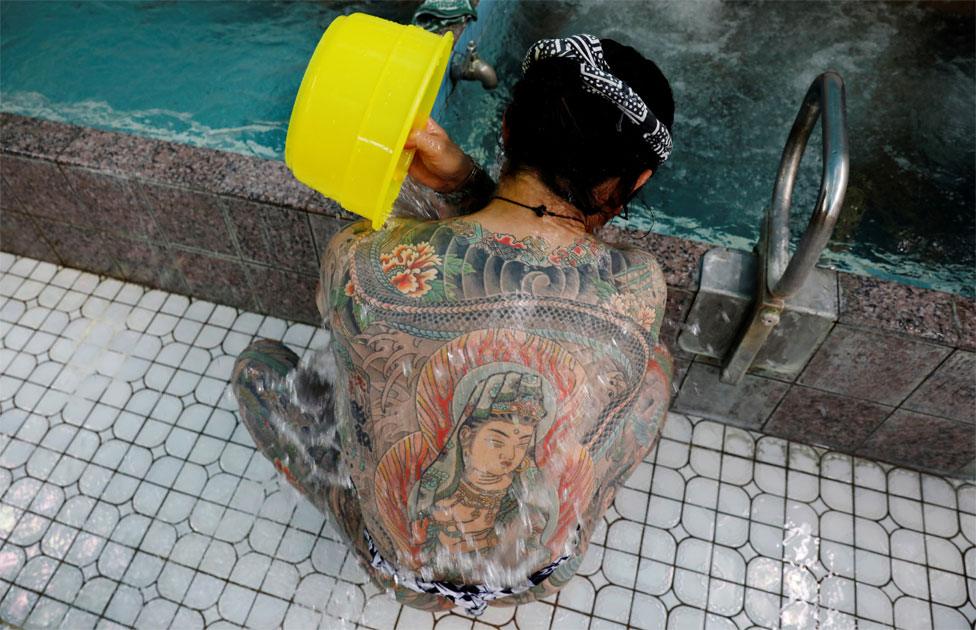 A man with body tattoos pours water over his back