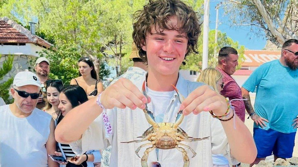 Harvey Owen in the middle of a gorup of people holding a crab by the pincers and smiling