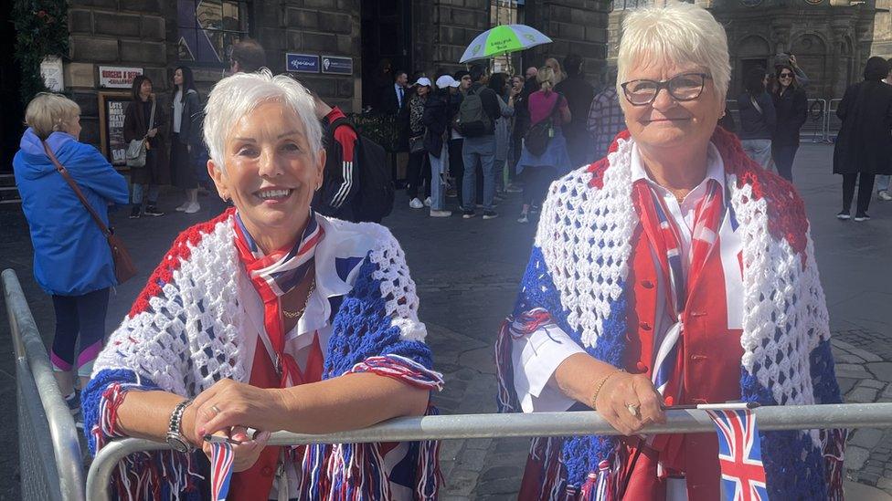 Two women leaning on a barrier with crocheted cardigans in red, white and blue in a Union Jack flag style.