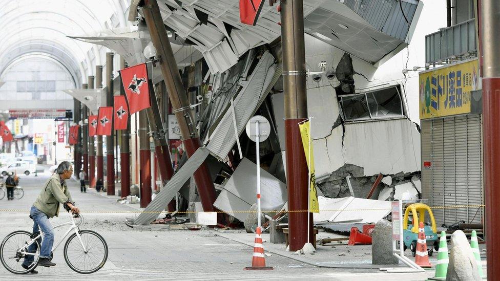 A cyclist looks at a shopping arcade destroyed by the earthquake in Kumamoto city, southern Japan.