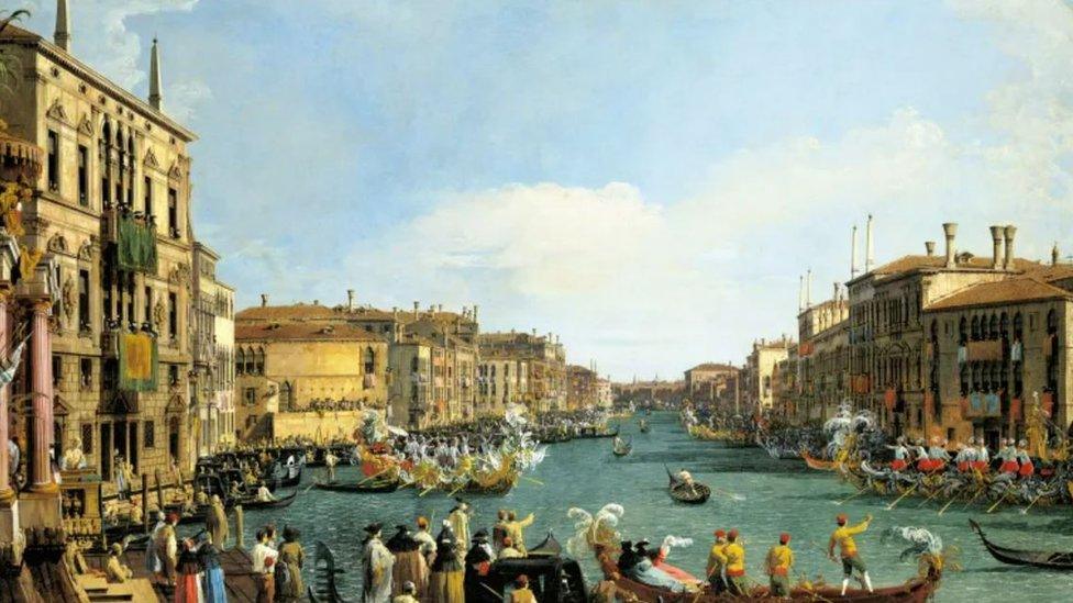 A painting by Canaletto of a river with buildings running down each side and people on boats