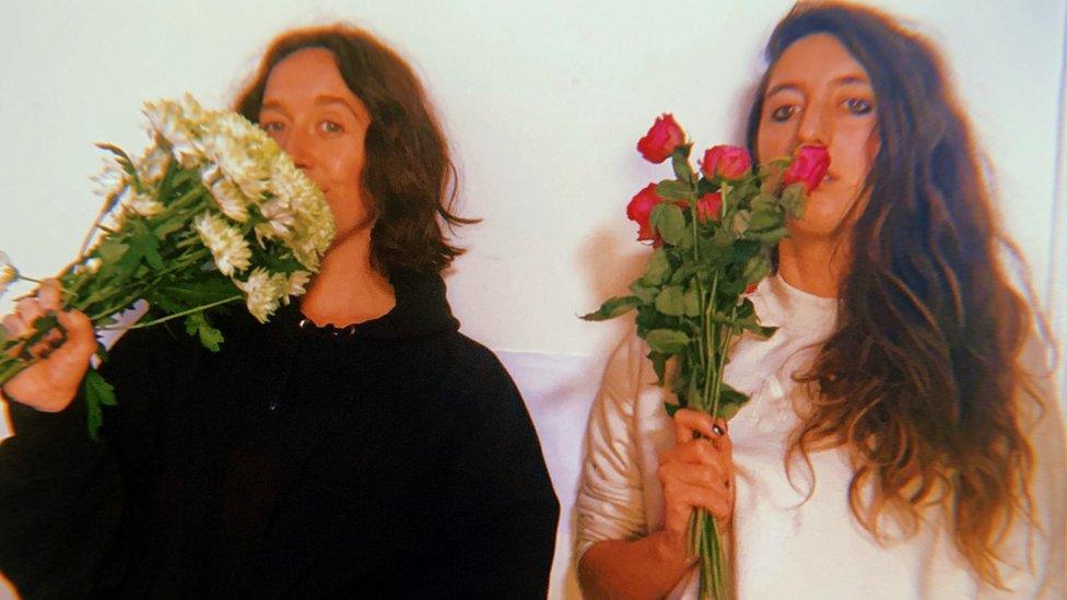 Bryony Ball and Meggan Baker looking at the camera holding flowers to their faces