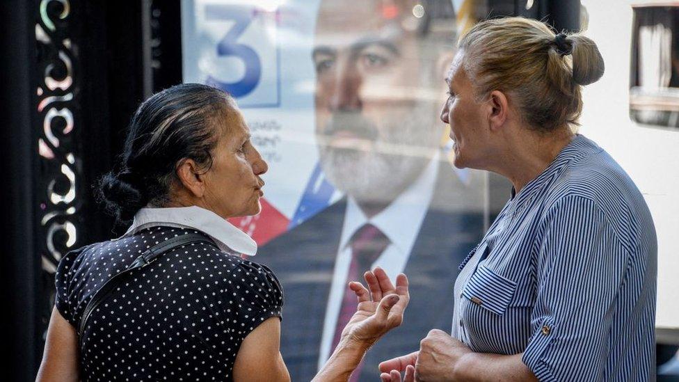 Two women speak by a campaign banner in Yerevan as Armenians vote in the June 2021 elections