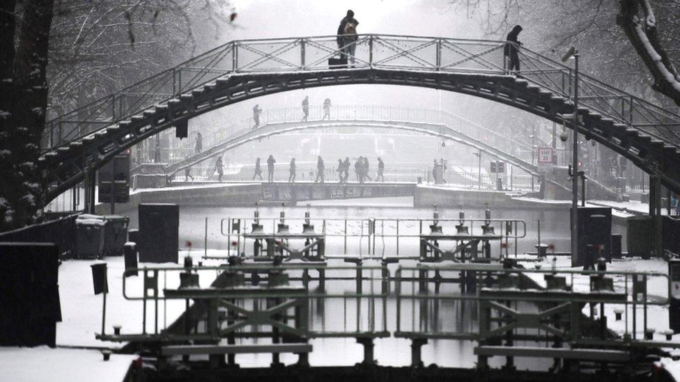 People use a footbridge to cross the canal Saint-Martin as snow falls over Paris on 22 January 2019