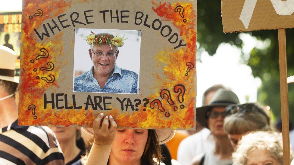 A protester in Sydney holds up a sign outside the Prime Minister's home showing a picture of Scott Morrison and a message: "Where the Bloody Hell Are Ya?"