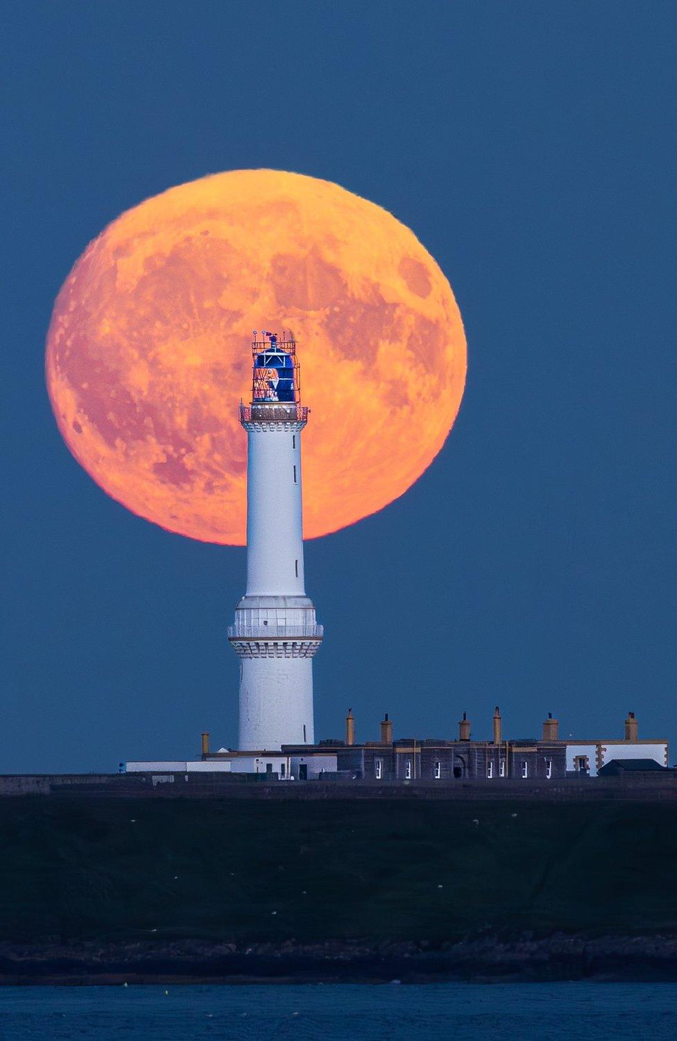 White lighthouse with an orange moon behind and an inky blue sky