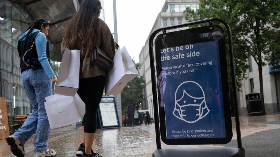 People walk past a sign advising mask wearing.