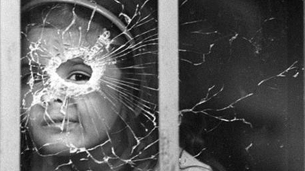 Girl looking through bullet-shattered window