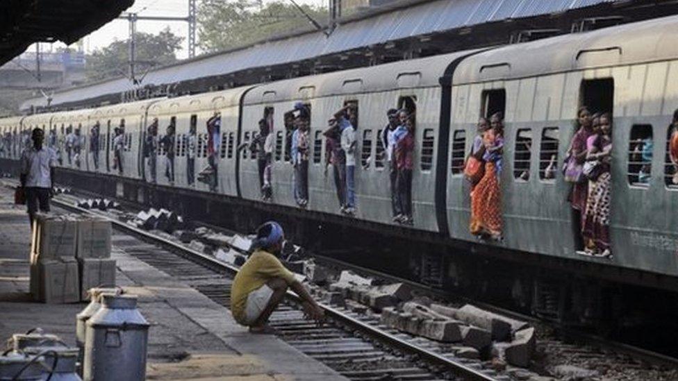 Indian passengers hang from the doors of the coaches of a crowded local train on the outskirts of Kolkata, India, Thursday, Feb. 26, 2015