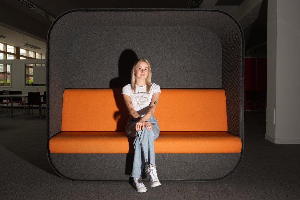 Lauren Kemsley sitting on an orange and black sofa at Harlow College