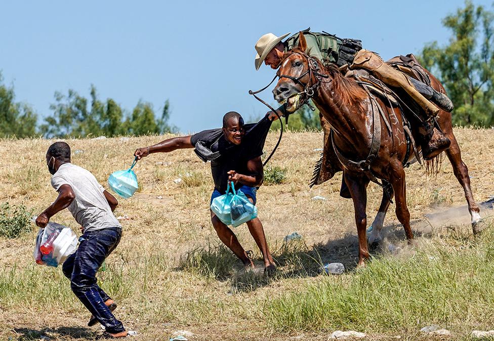 A US Border Patrol agent on horseback tries to stop a Haitian migrant from entering an encampment.