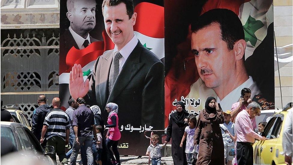 Syrians walk past billboards of Bashar al-Assad and his father in Damascus (file photo)