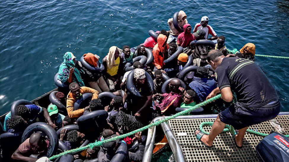 An illegal migrant vessel is tied on to the Tunisian coast guard patrol boat before its passengers are asked to disembark