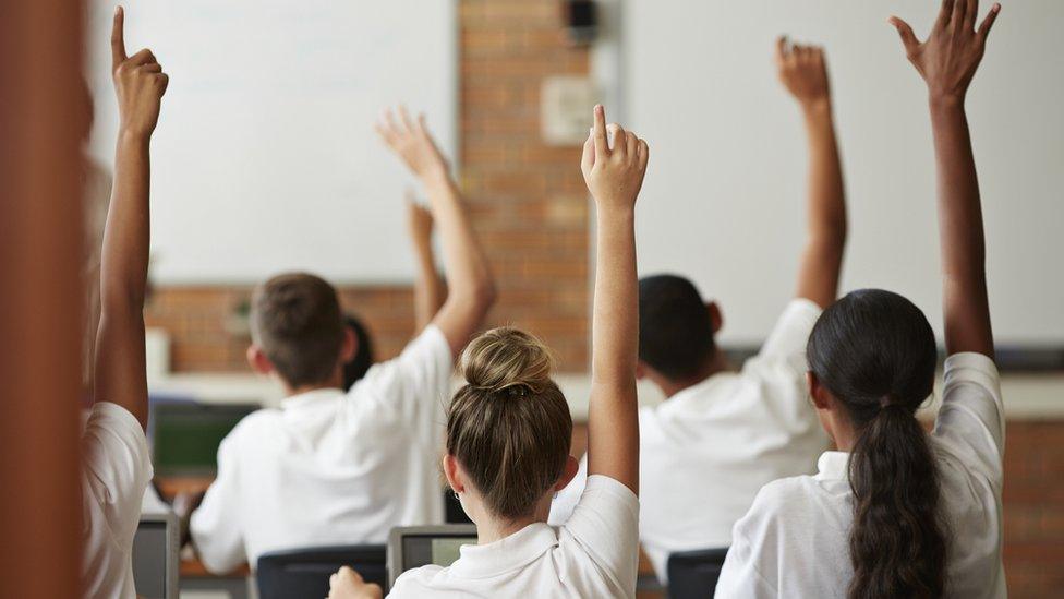 children in classroom raising their hands