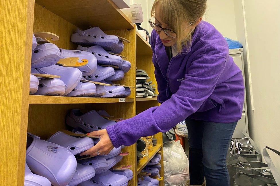 A woman sorts Croc shoes on shelves