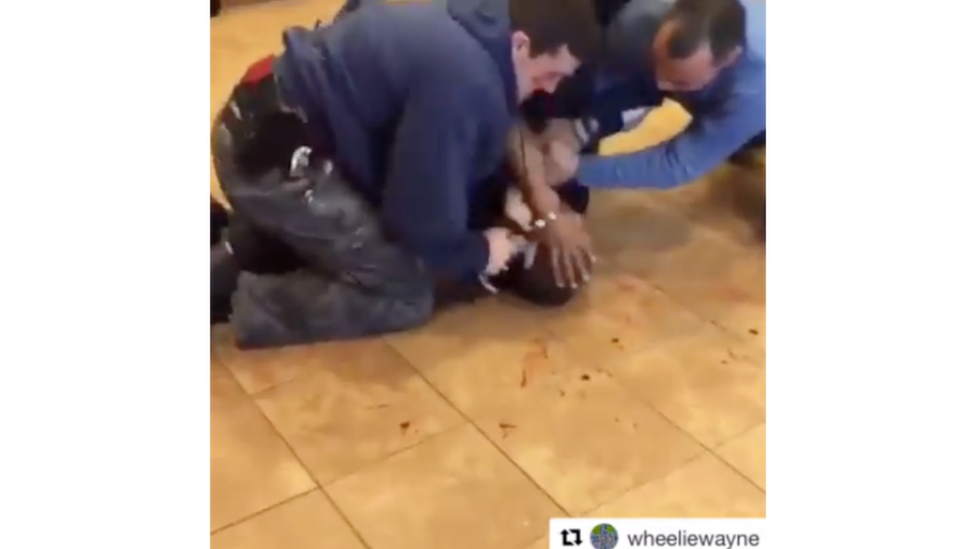 White policemen hold down a black man on a blood spattered floor