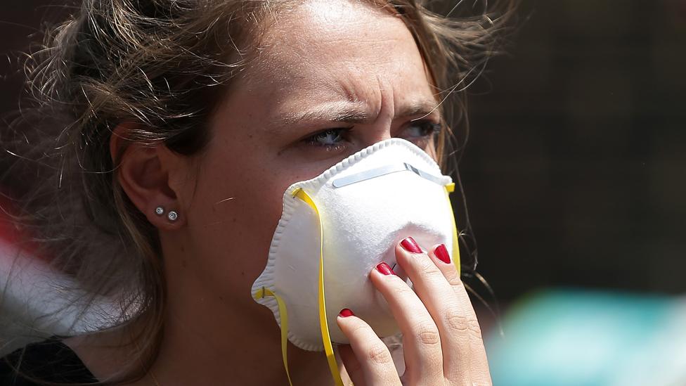 A woman wears a mask as she waits near a Grenfell Tower, a residential block of flats in west London on June 14, 2017, as firefighters continue to control a fire that started in the flats in the early hours of the morning.