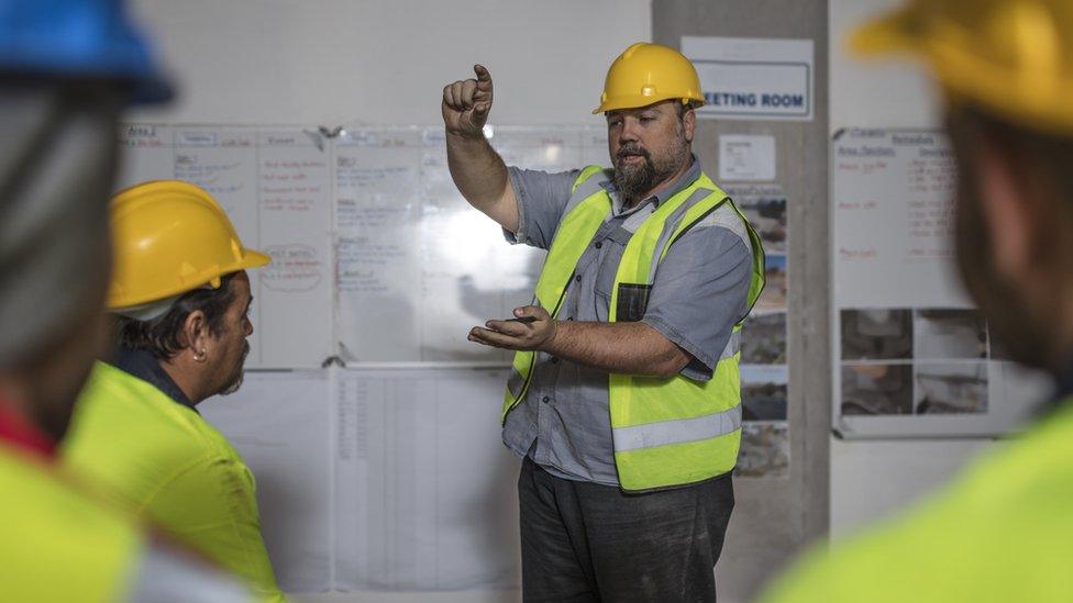 Construction worker trains others with whiteboard behind