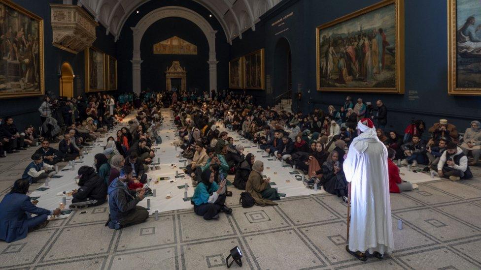 people watch white-robed man speak at V&A