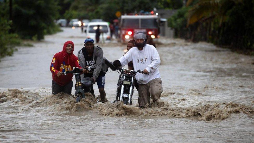 People cross a flooded road as a result of the intense rains, in San Jose de Ocoa, Dominican Republic 18 November 2023.