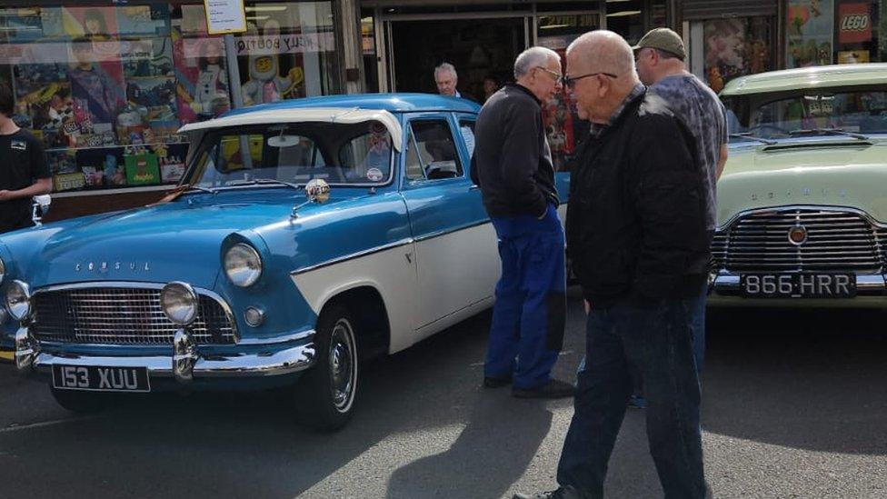 Three men standing next to a blue 1950s Ford Consols