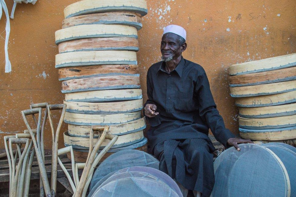 A man sits selling sieves