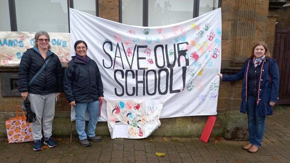 Three women holding a "save our school" banner