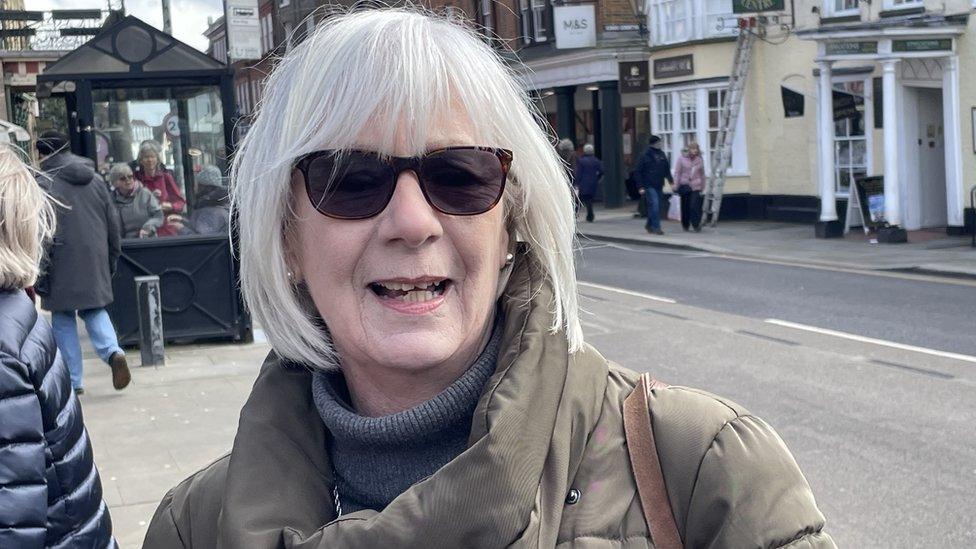 Woman with medium-length blonde hair and glasses stands in a street