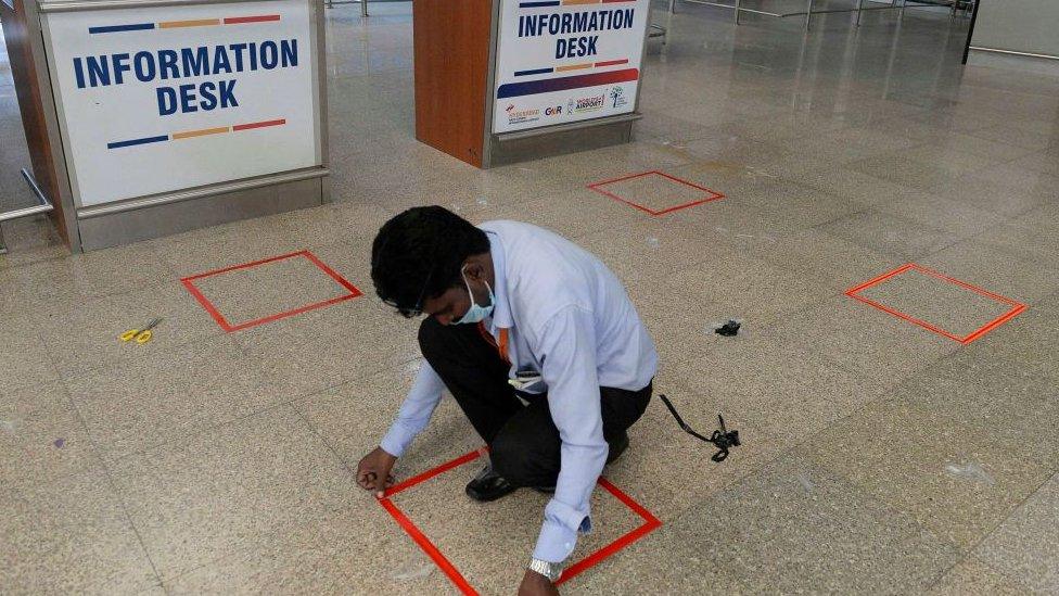 A worker marks a square on the ground to mark social distancing