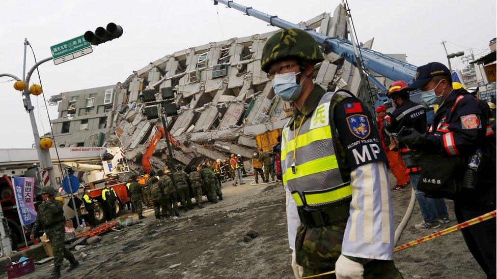 A soldier stands guard in front of a collapsed building after an earthquake hit Tainan, southern Taiwan