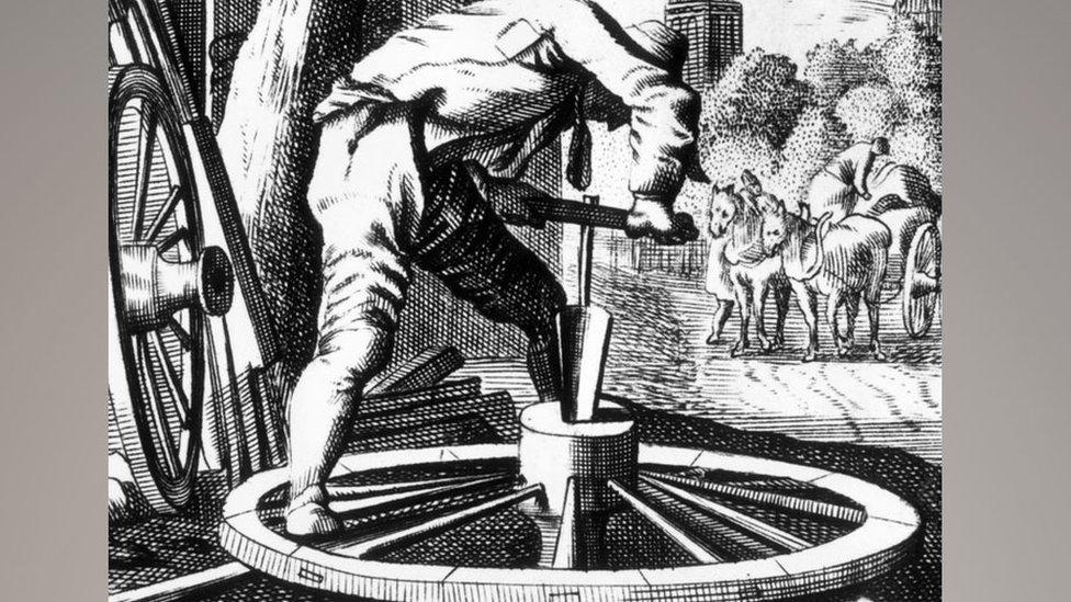 A black and white drawing of a 17th Century wheelwright bending over a wheel with a tool