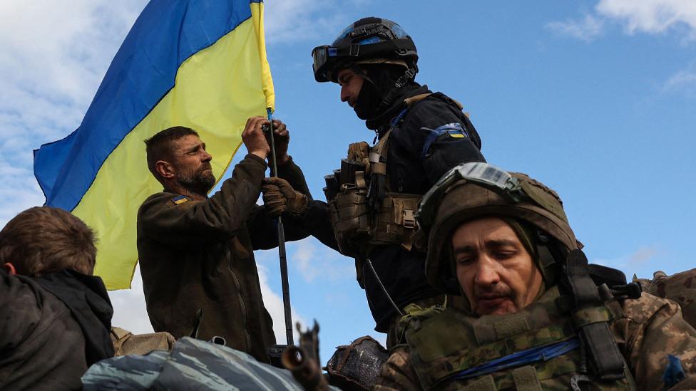 Ukrainian soldiers adjust a national flag atop a personnel armoured carrier on a road near Lyman, Donetsk, in October 2022