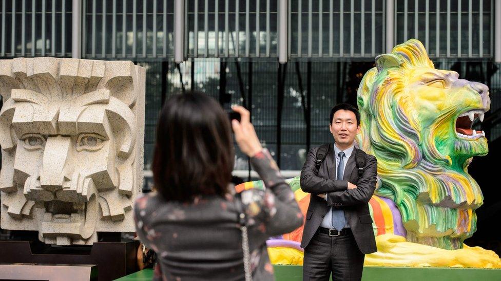 A man poses in front of a lion (R) painted in rainbow stripes displayed next to a sculpture of a lion head (L), dating back to the 1930s, outside HSBC"s main office in Hong Kong on December 6, 2016.