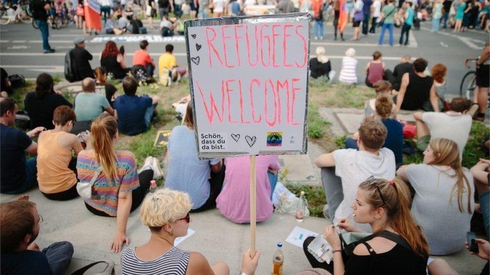 People taking part in a demonstration hold a sign that reads "refugees welcome"