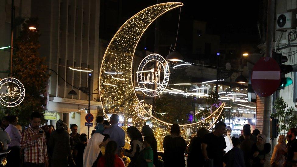 Shoppers in Amman, Jordan walk past a giant Crescent Moon and other light decorations