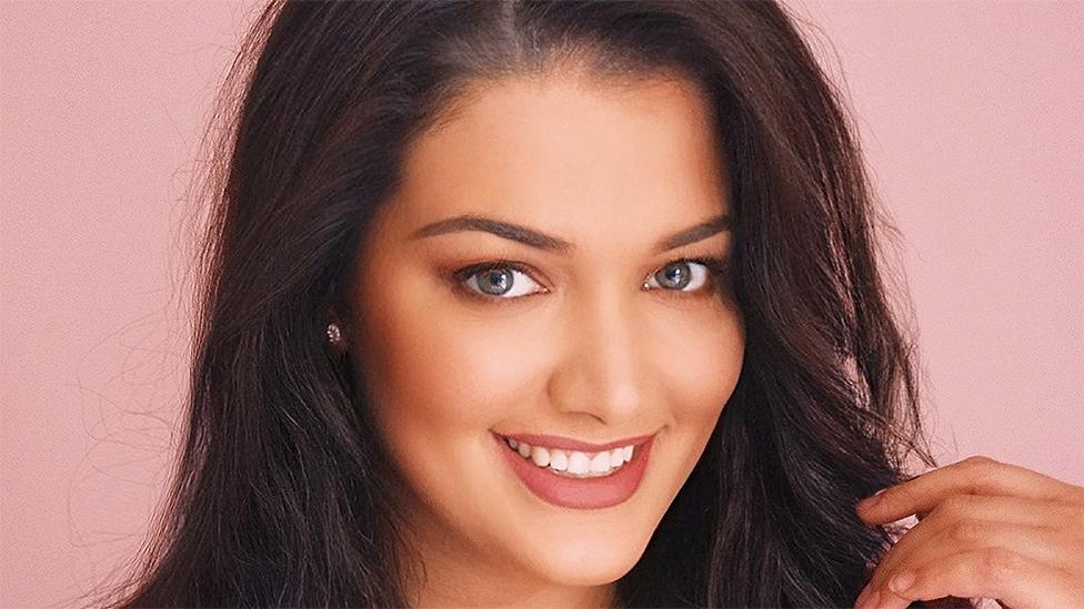 A close-up headshot photograph of Abigail who has dark brown hair. She is smiling and is looking straight at the camera