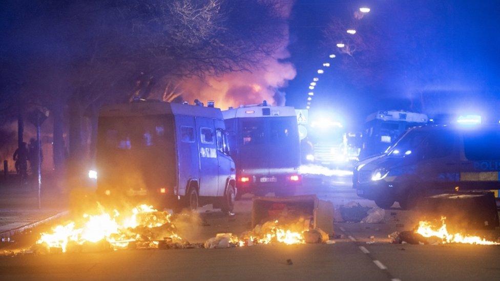 Police vans break up a crowd of protesters while a bus burns in the Rosengard area of Malmo