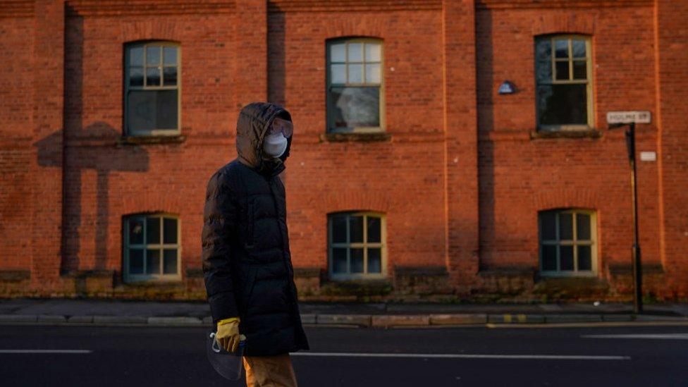 A masked man walks alone in a city