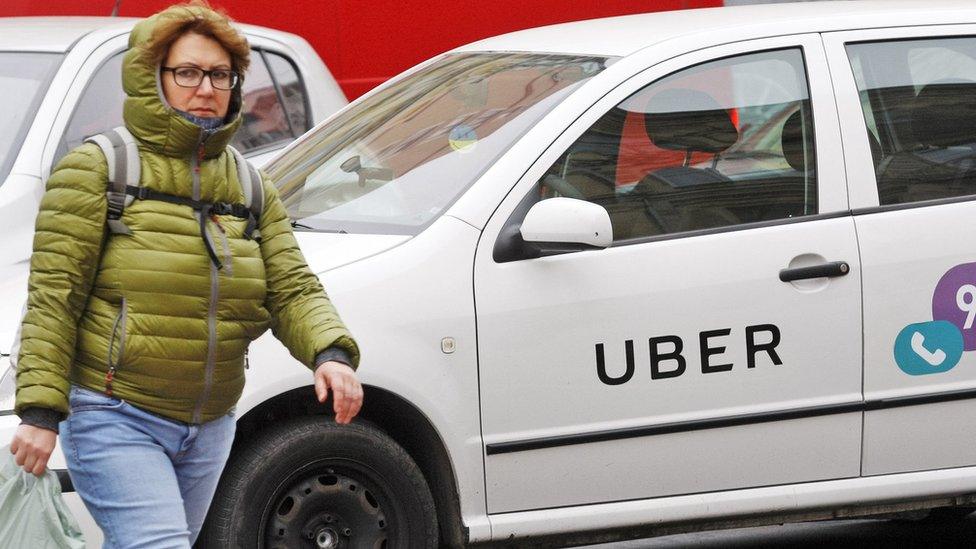 A woman seen walking next to a white car with a logo of Uber taxi cab company in Kiev, Ukraine.