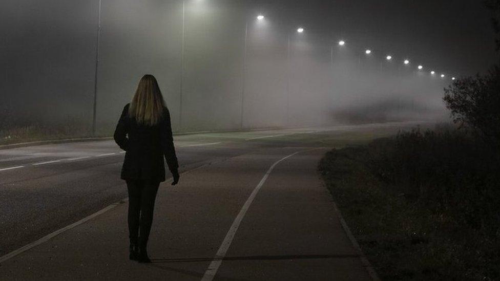 Woman walking along street lit by street lights