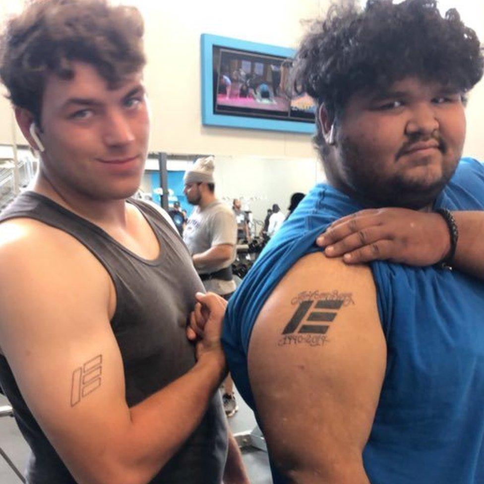 Two men show off tattoos on their upper arms. Both tattoos are of the Etika logo which looks like a large capital e.