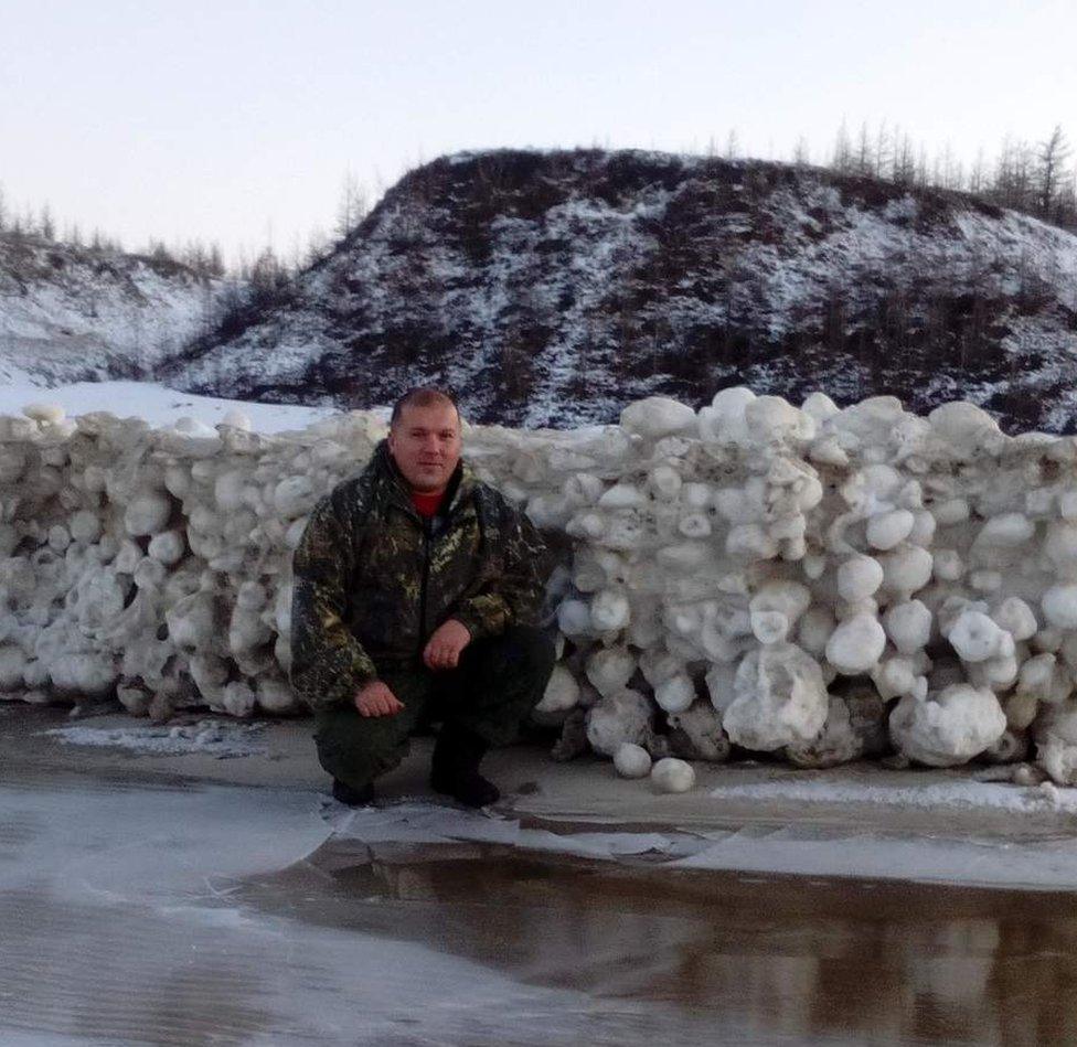 A picture of Alexei Primak crouching by a "snowball wall" formed from the icy spheres.