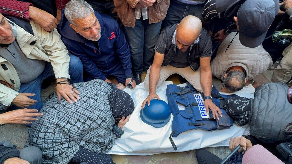 Mourners in Gaza gather around the body of cameraman Samer Abudaqa which has been covered in a white sheet with a press vest and helmet