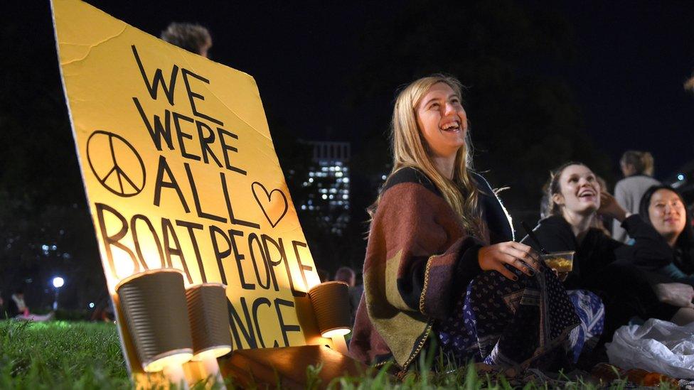 Protesters sit next to a placard and candles to remember Syrian child Aylan Kurdi, who drowned in Turkey last week creating an international outcry, during a vigil in Sydney on September 7