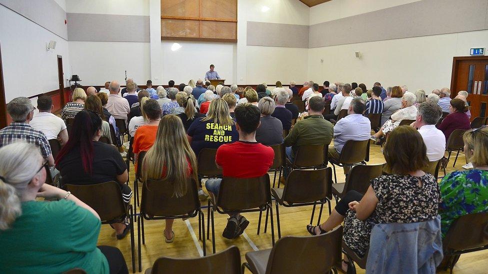 A crowd of people sit in a Presbyterian church listening to the minister speak at a prayer vigil